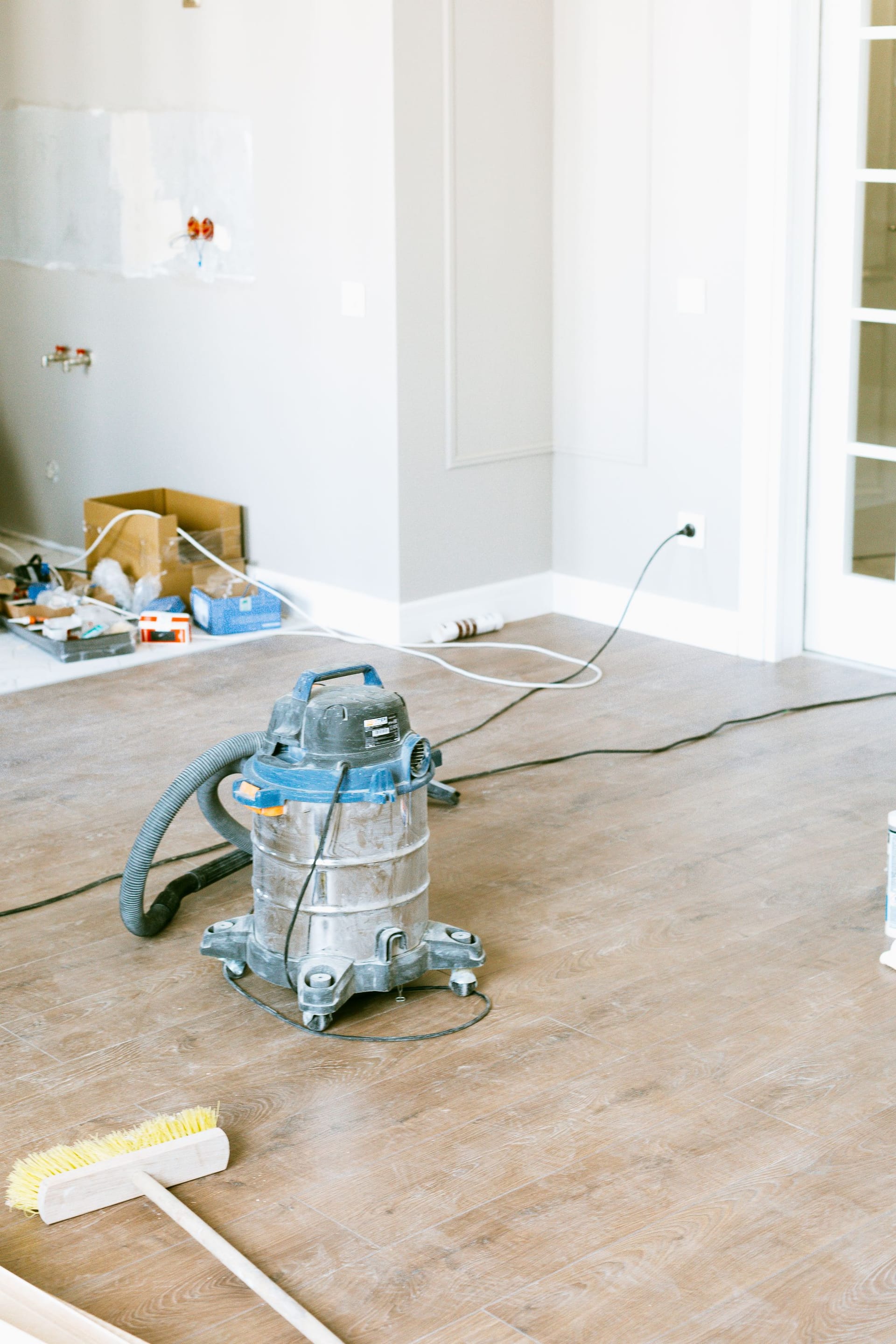 A shop vacuum and push broom on the floor of a house still under construction